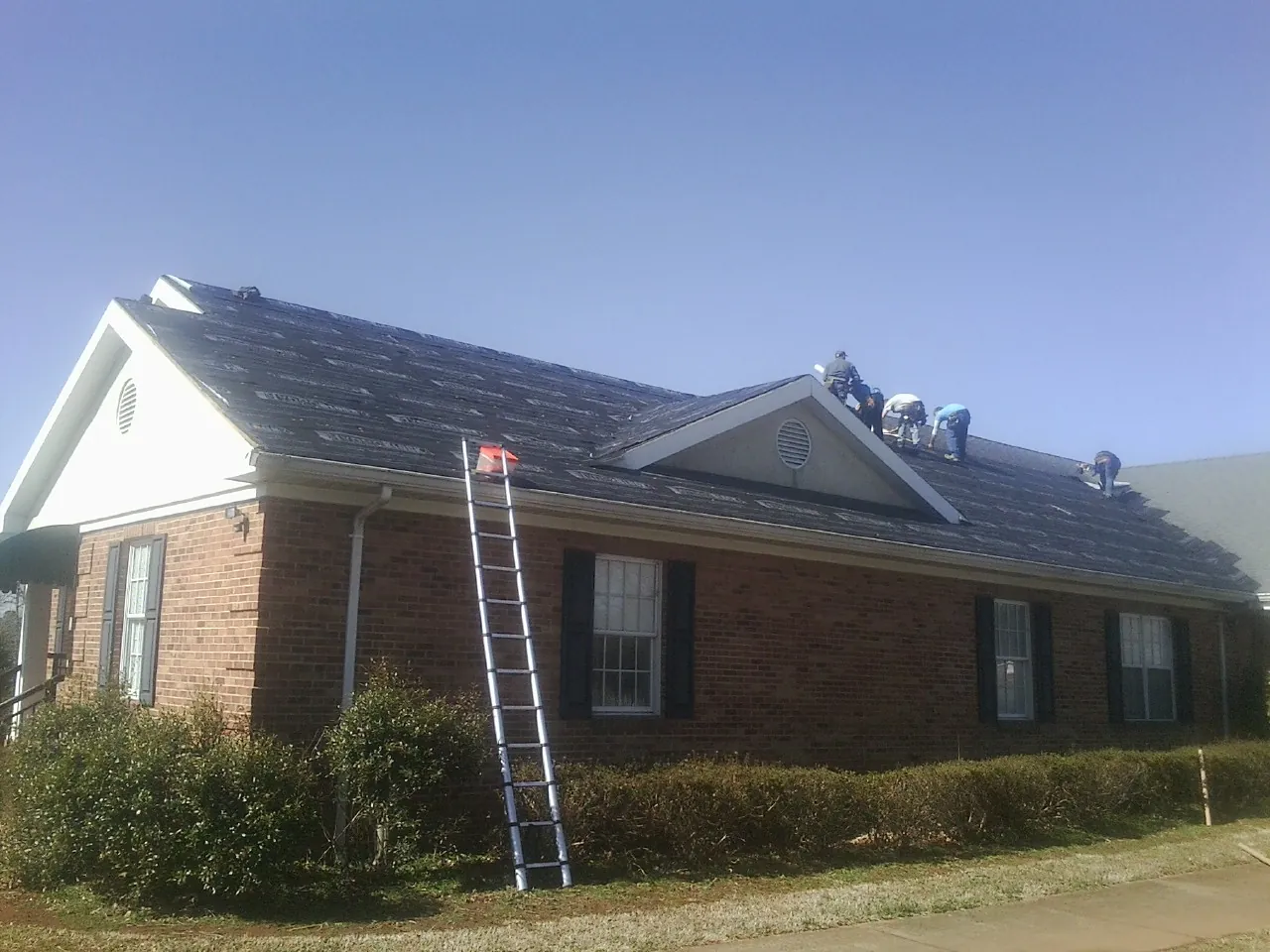 Crew tearing shingles off a brick ranch roof with a ladder set — Metal Roof Repair work by our crew in Bloomingburg