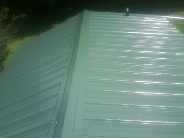 New green metal panels meeting at the ridge of a roof — Flat Roof Repair work by our crew in Bloomingburg