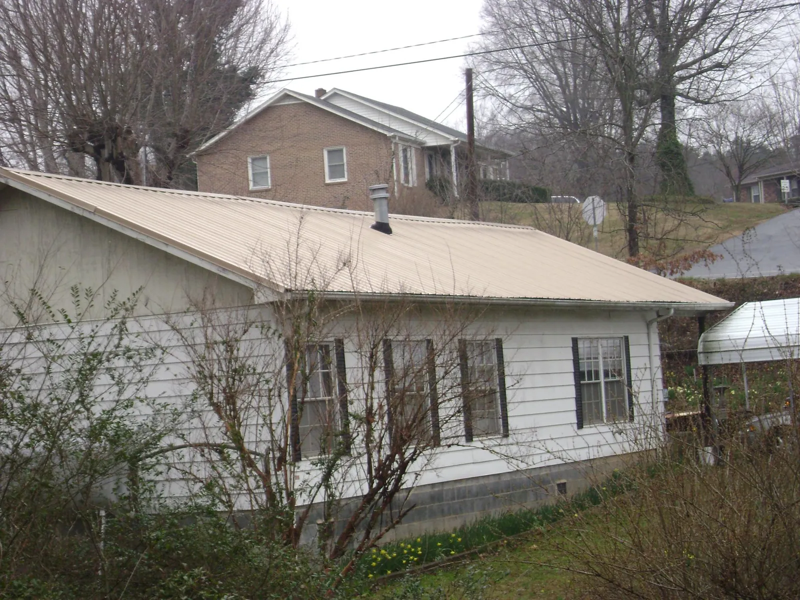 Tan metal roof on a white sided house set into a hillside — Commercial Roofing by Roofing Brothers in Bloomingburg